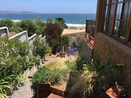 Un balcón con vista al océano, rodeado de plantas diversas y un pequeño rincón con asientos.