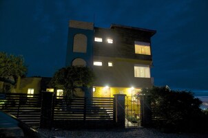 Un edificio de varios pisos con una torre destacada, una entrada con portones y una fachada bien iluminada.