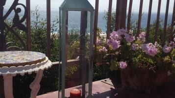 Un balcon doté d’une balustrade en fer forgé, d’une lanterne, d’une table dont le plateau est orné de motifs et d’un pot de fleurs contenant des fleurs roses.
