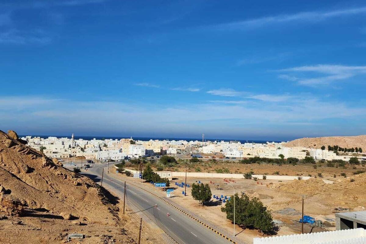A coastal town with white buildings, a clear sky, and a road leading towards the sea.