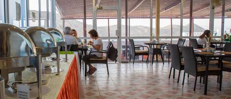 A restaurant with a buffet setup, large windows, and a tiled floor.