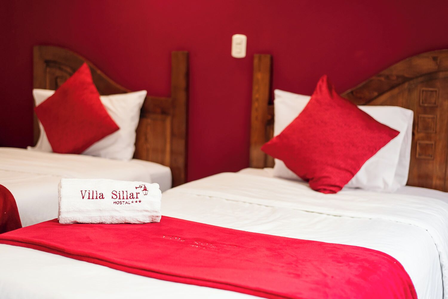 Zwei Betten mit roten Kissen und ein weißes Handtuch mit dem Logo von Villa Sillar.