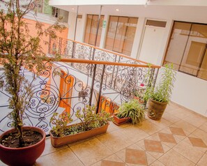 Un espacio interior amplio con suelo de baldosas, barandilla de metal con diseños elaborados y varias plantas en macetas.