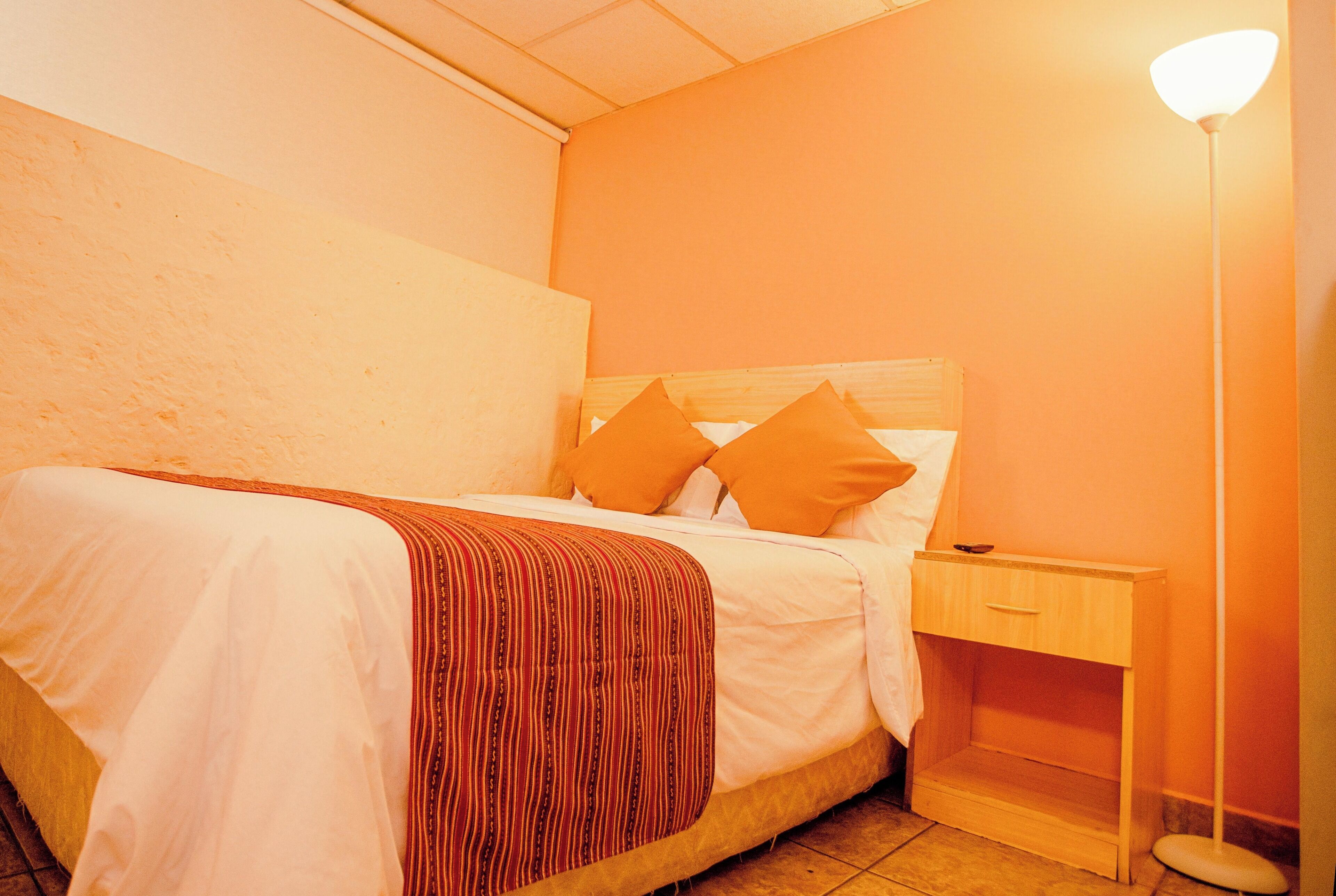 Een net opgemaakt bed met een gestreept dekbed en twee kussens, een nachtkastje met een lamp, en een houten nachtkastje.