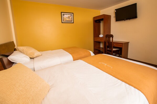 Una habitación de hotel con dos camas, un escritorio de madera, una silla y un televisor en la pared.