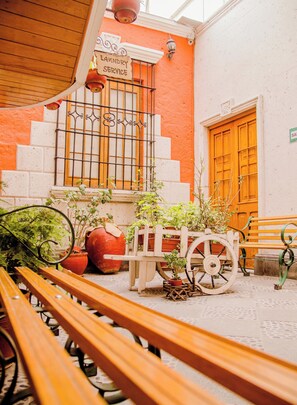 Un patio con bancos de madera, un cartel de servicio de lavandería, un carro de madera con plantas en macetas y una puerta naranja grande.