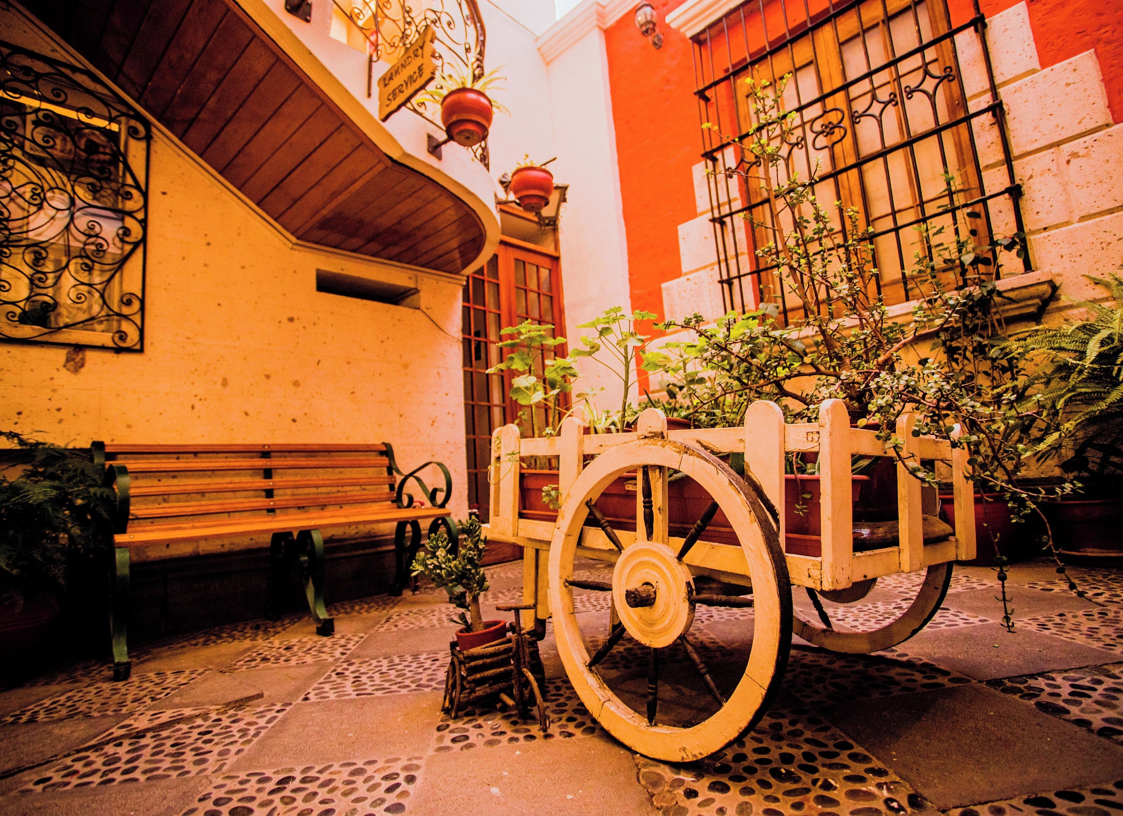 A narrow alley with a wooden bench, a cart, and potted plants.