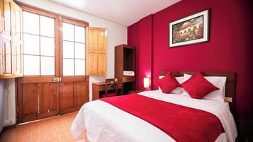 Habitación de hotel con una cama grande, un armario de madera, un escritorio y una pared roja.