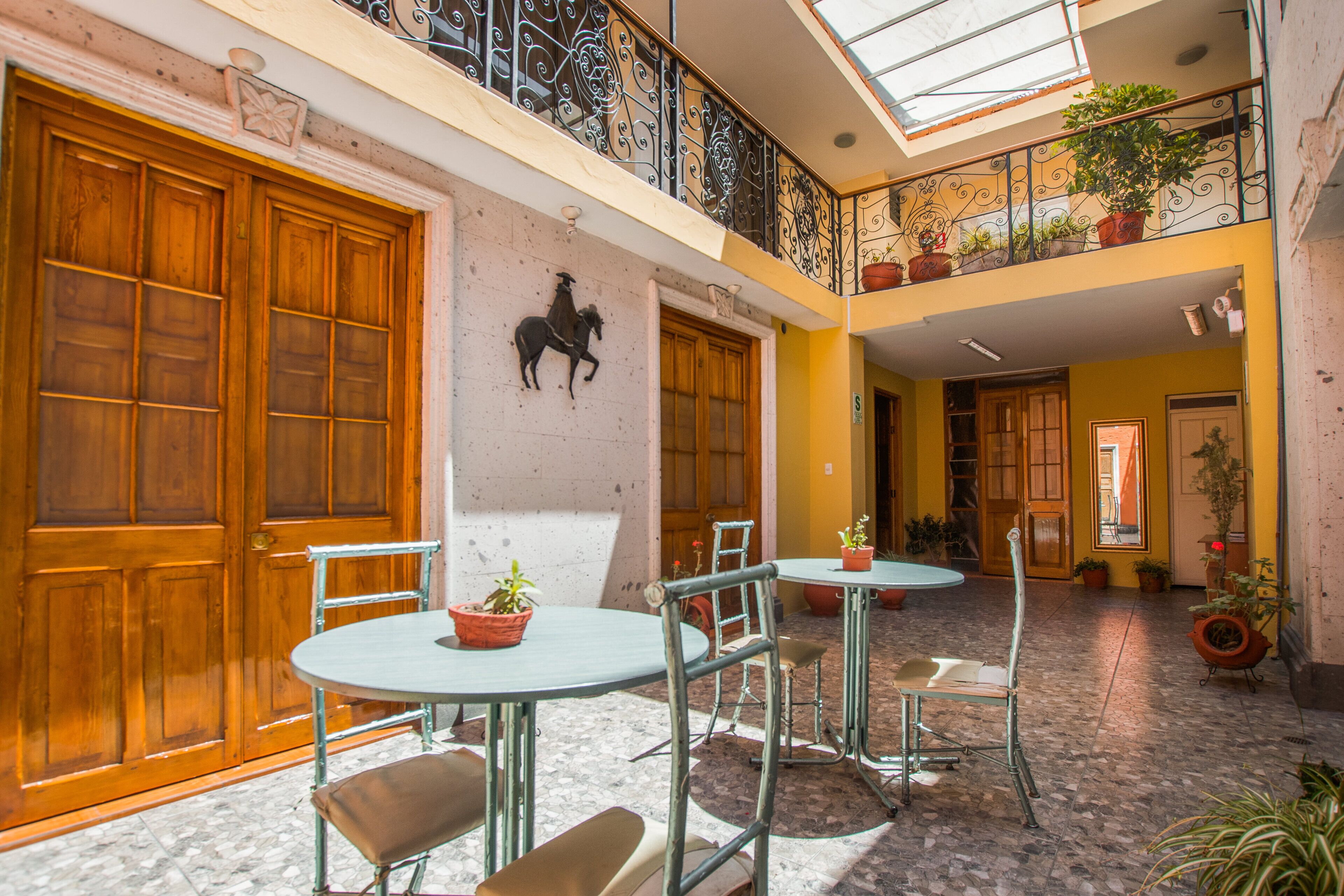 A courtyard with wooden doors, a round table with chairs, and potted plants.