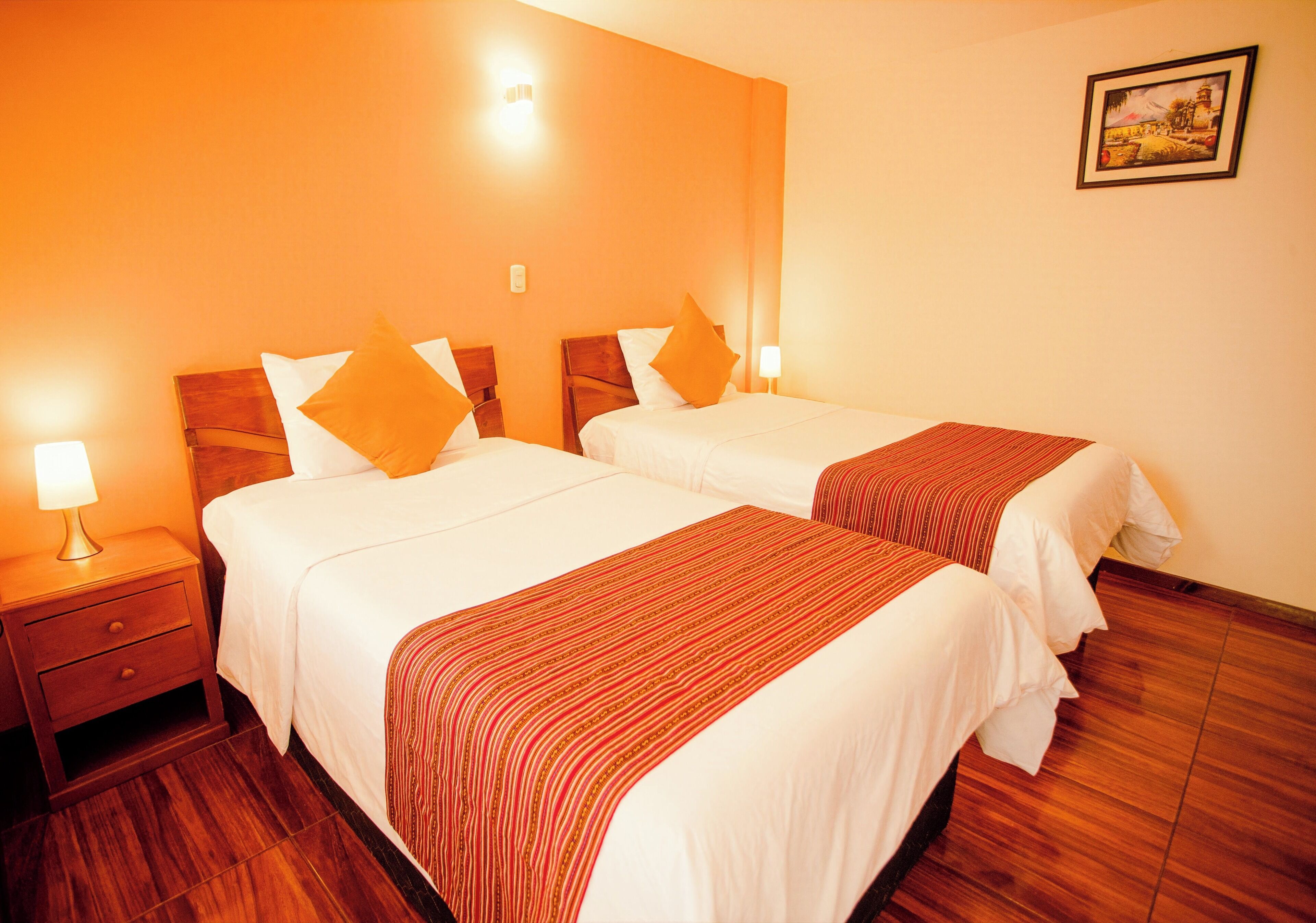 A hotel room with two beds, wooden headboards, a nightstand with a lamp, and a framed picture on the wall.