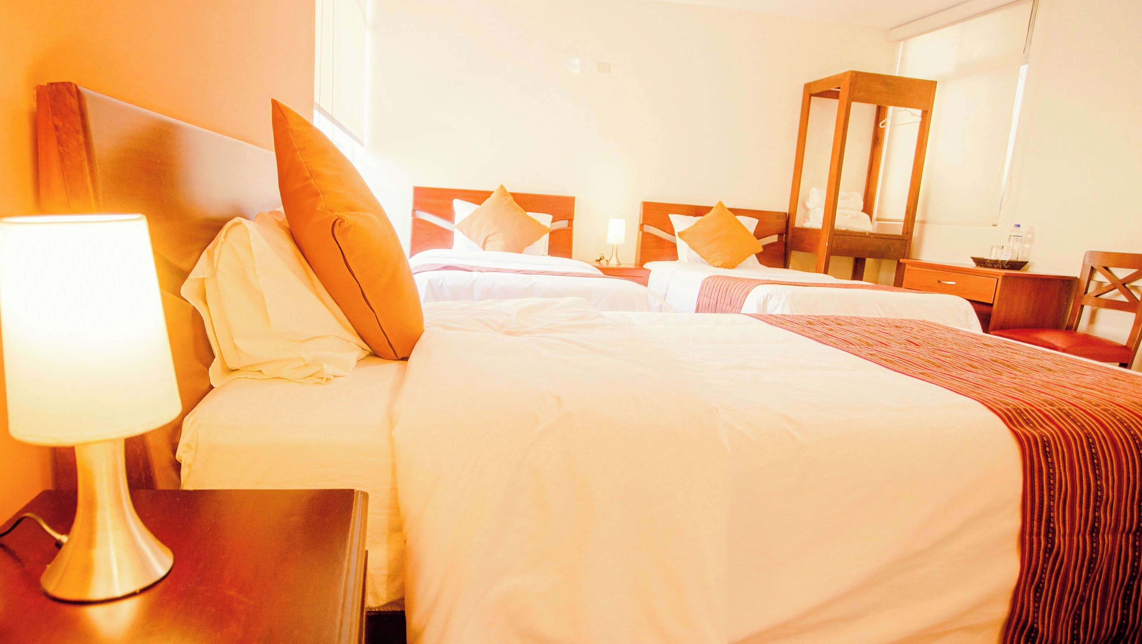 Una camera d'albergo con due letti, un comodino con una lampada, una sedia di legno e uno specchio.