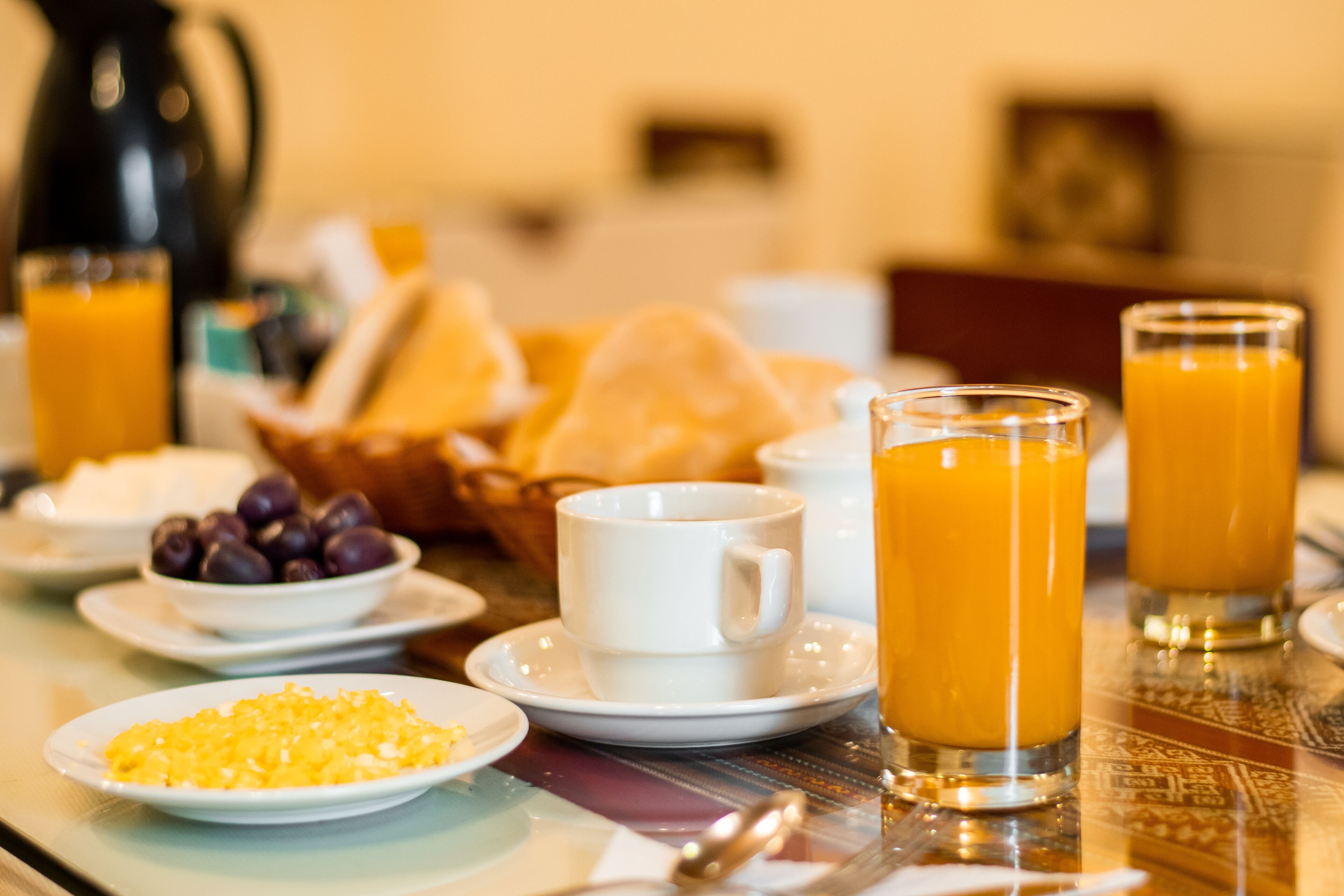 A breakfast table with plates of food, glasses of orange juice, and a coffee pot.