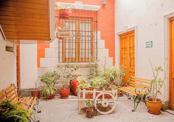 Un patio con un banco de madera, plantas en macetas, un letrero de servicio de lavandería y una puerta con la inscripción 'SALIDA'.