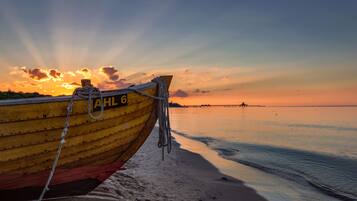 Een boot afgemeerd aan een zandstrand, met een ondergaande zon op de achtergrond.