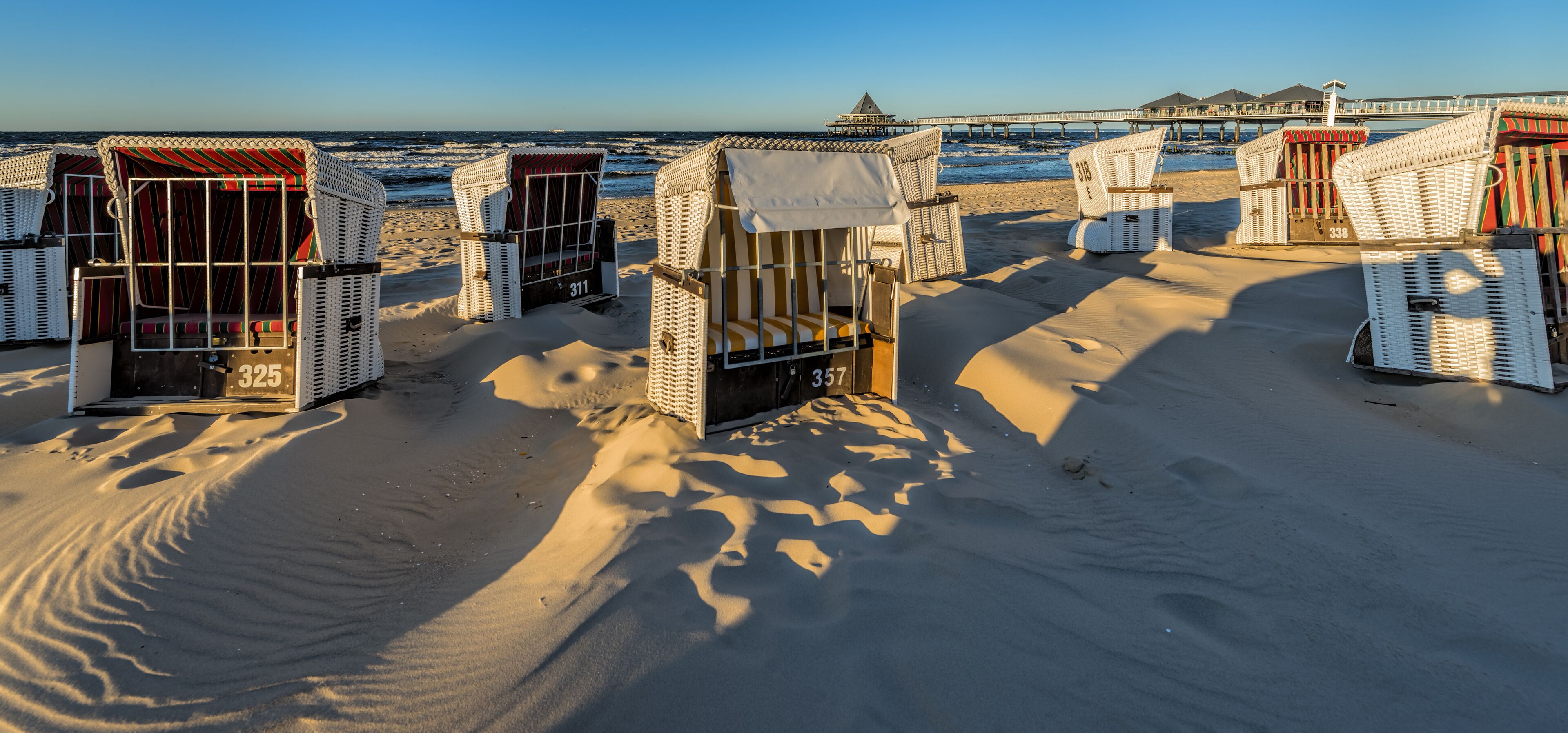 Des cabanes de plage numérotées, une jetée et l’océan en arrière-plan.