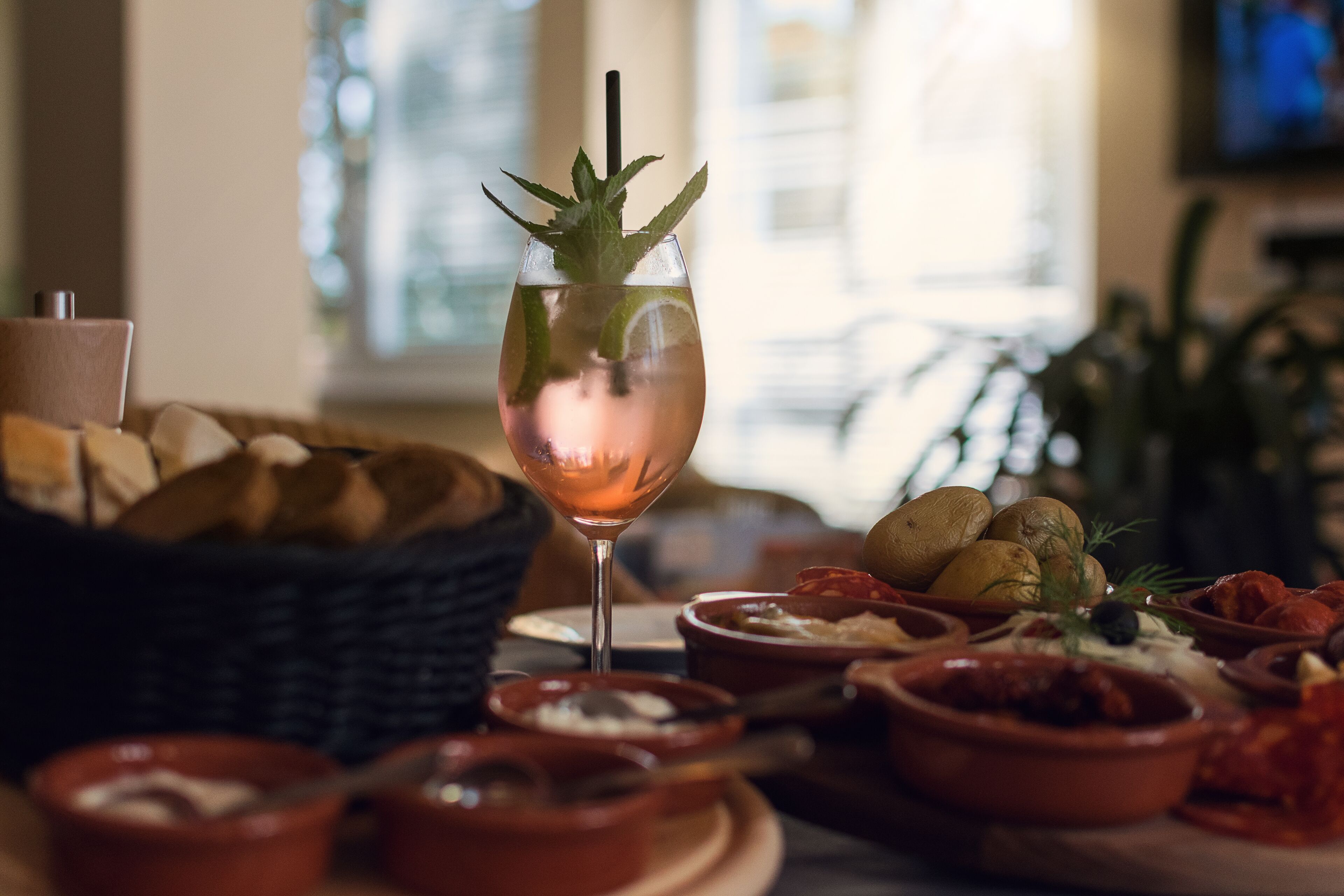 Een tafel met een glas rosé wijn, versierd met munt, omringd door verschillende gerechten en brood.