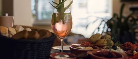 A table with a glass of rosé wine garnished with mint, surrounded by various dishes and bread.