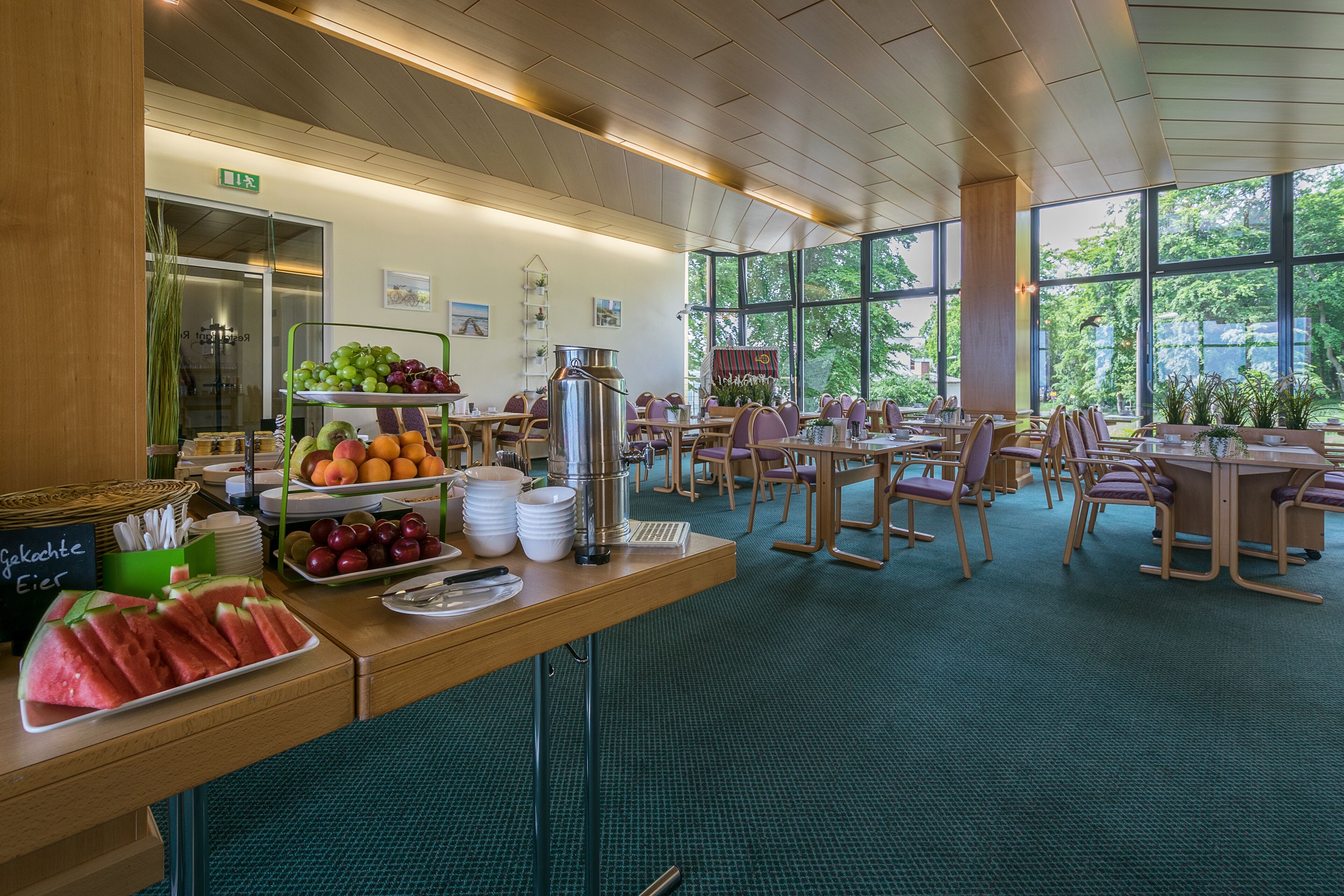 Un bufé de desayuno con diversas frutas, una estación de café y diferentes disposiciones de mesas y sillas.