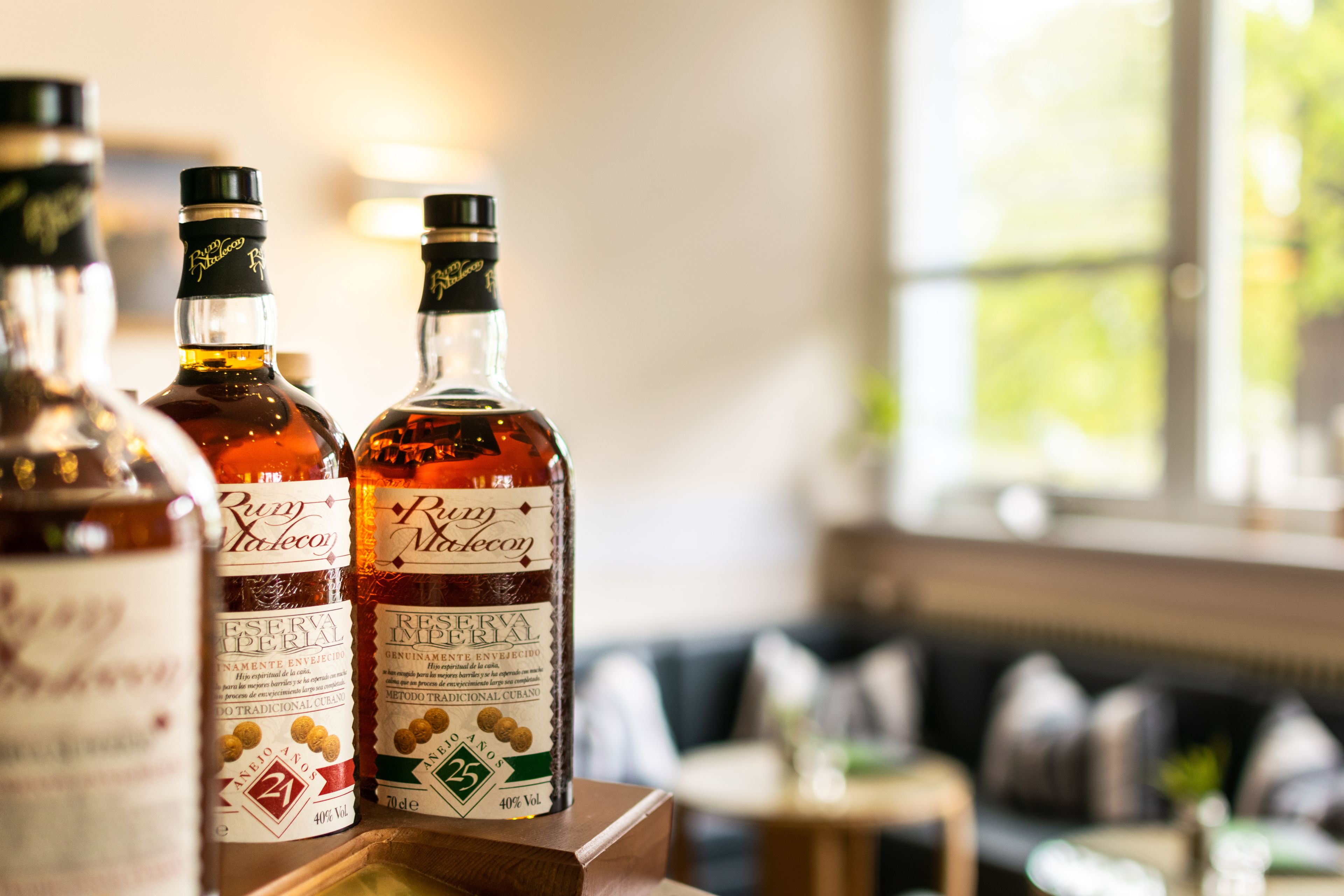 Drie flessen Rum Regal op een houten tafel in een goed verlichte kamer met een groot raam en een bank op de achtergrond.