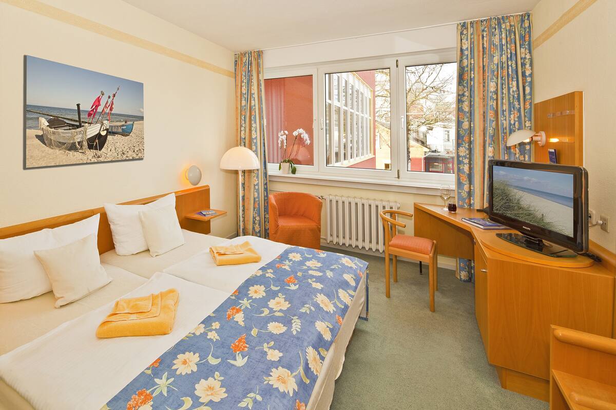 A hotel room with a bed, a desk, a chair, a television, and a window with curtains.