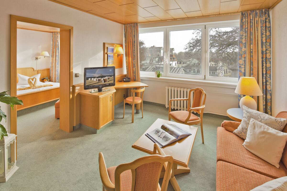 A hotel room with a bed, desk, computer, chair, sofa, and a view of the city through the window.