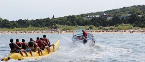Un radeau jaune transportant des passagers est remorqué par un bateau à moteur sur une étendue d’eau.