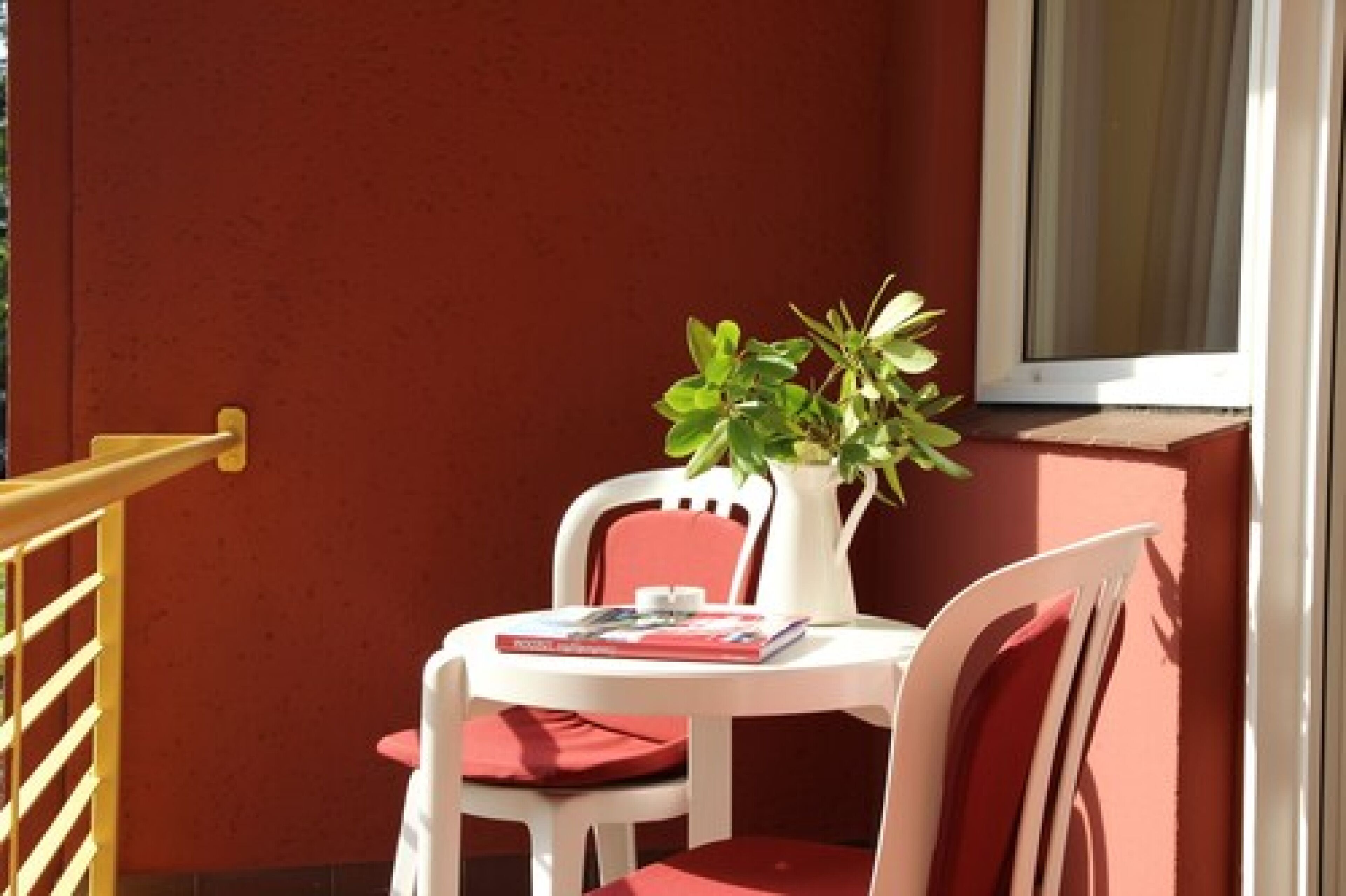 A small balcony with a white table and two chairs, a potted plant, and a window with a view.