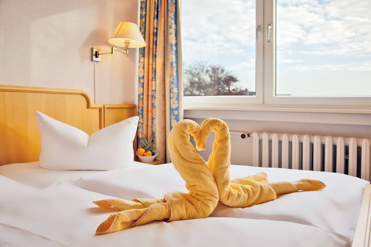 A hotel room with a bed, a lamp, curtains, and a view of the sky.