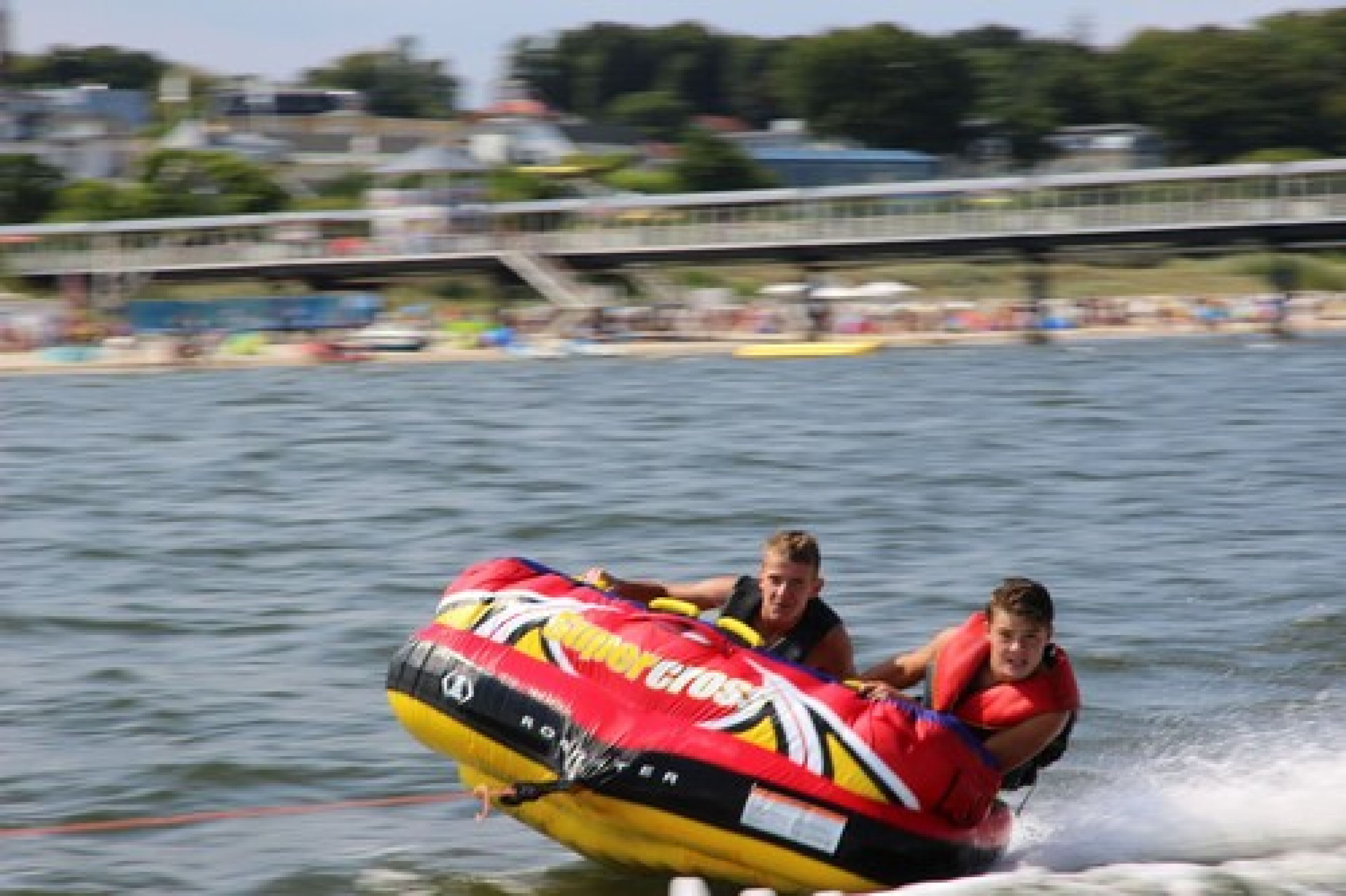 Une activité nautique consistant à faire de la bouée tractée par un bateau, avec une personne sur une bouée gonflable rouge et jaune.