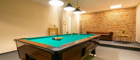 A pool table with balls, a brown leather sofa, and a small table with a plant.