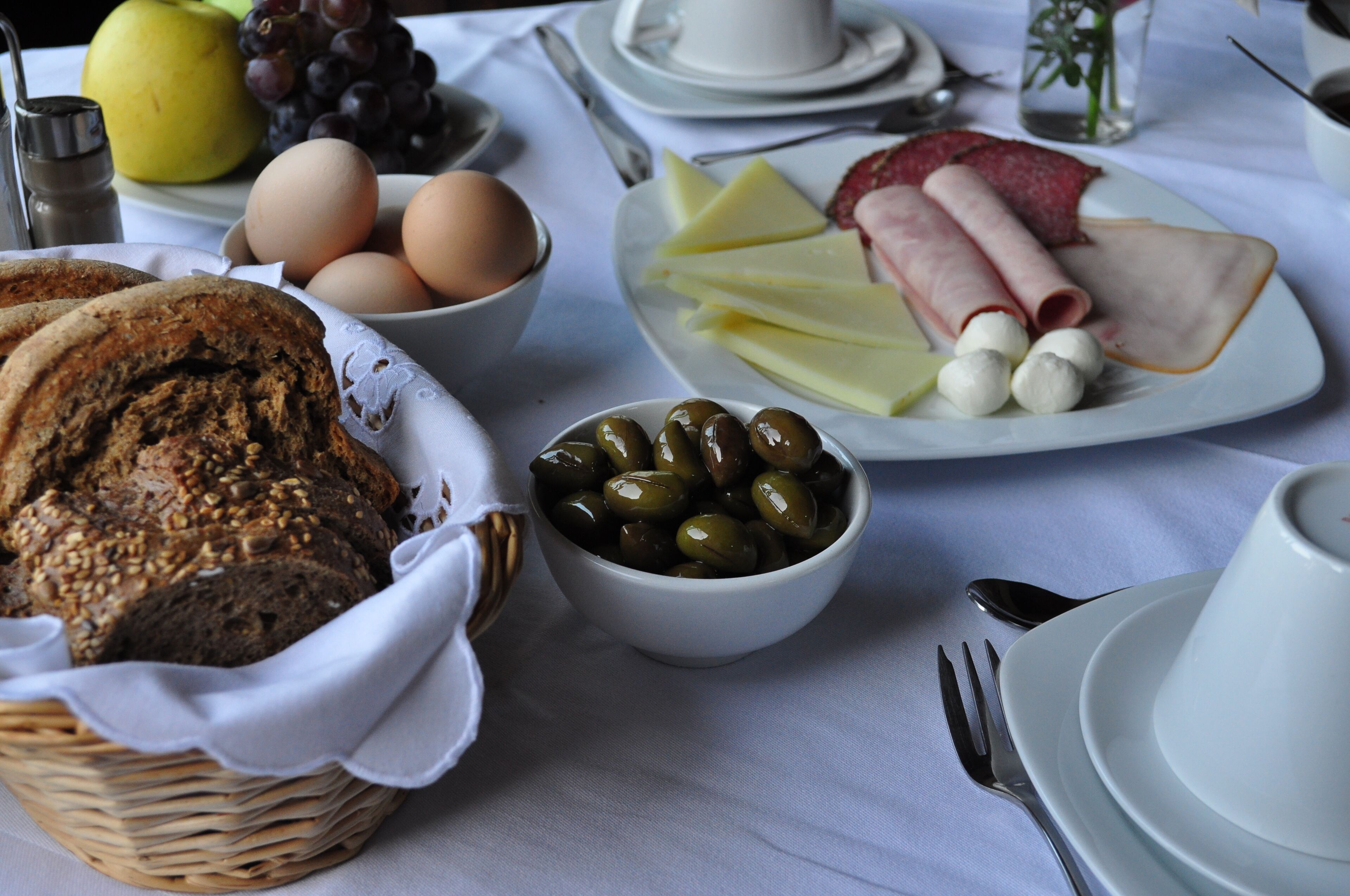 A table set with bread, eggs, cheese, olives, and ham.