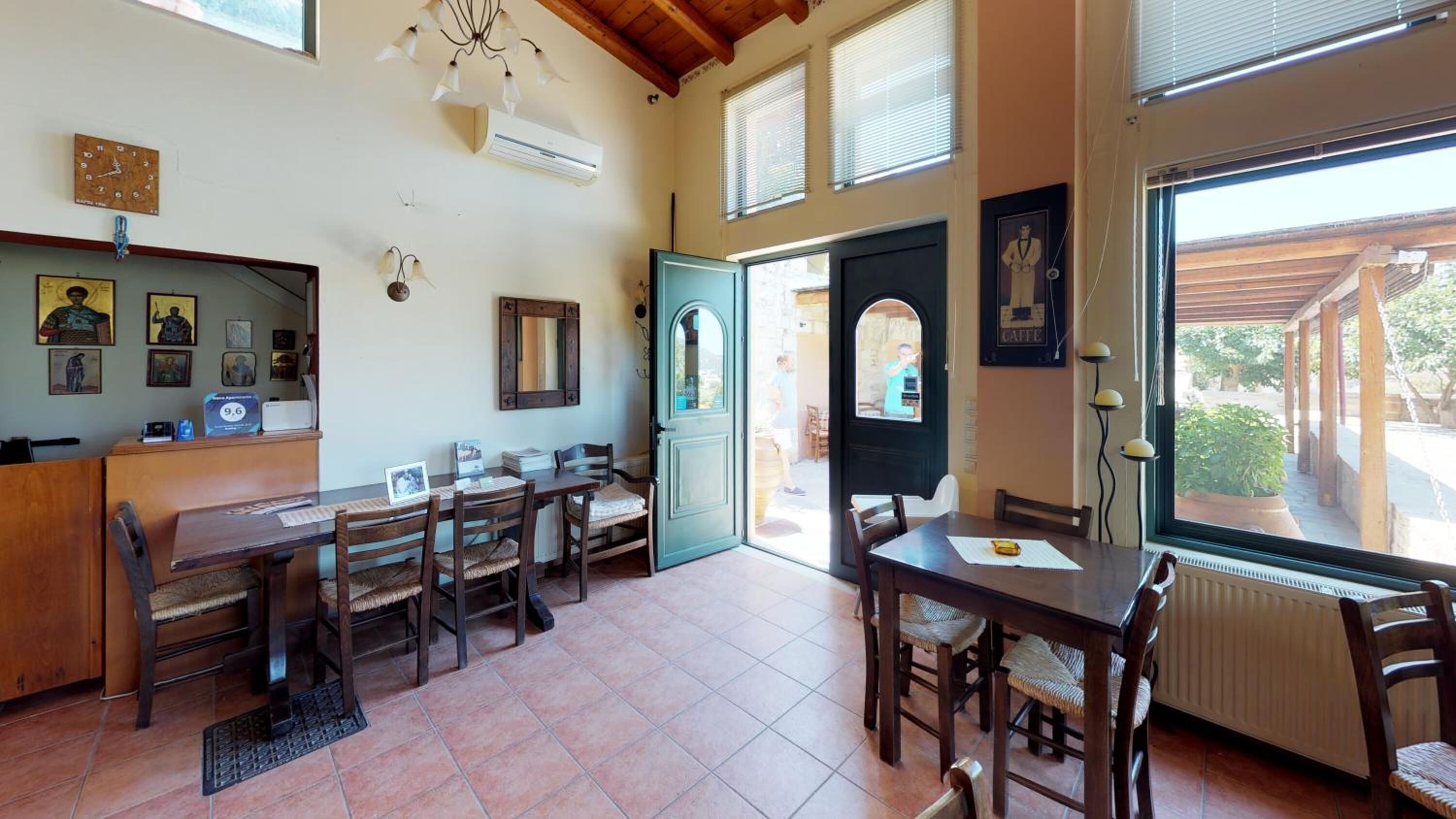 A dining area with wooden tables and chairs, a large window with a view of the outdoors, and a door leading outside.