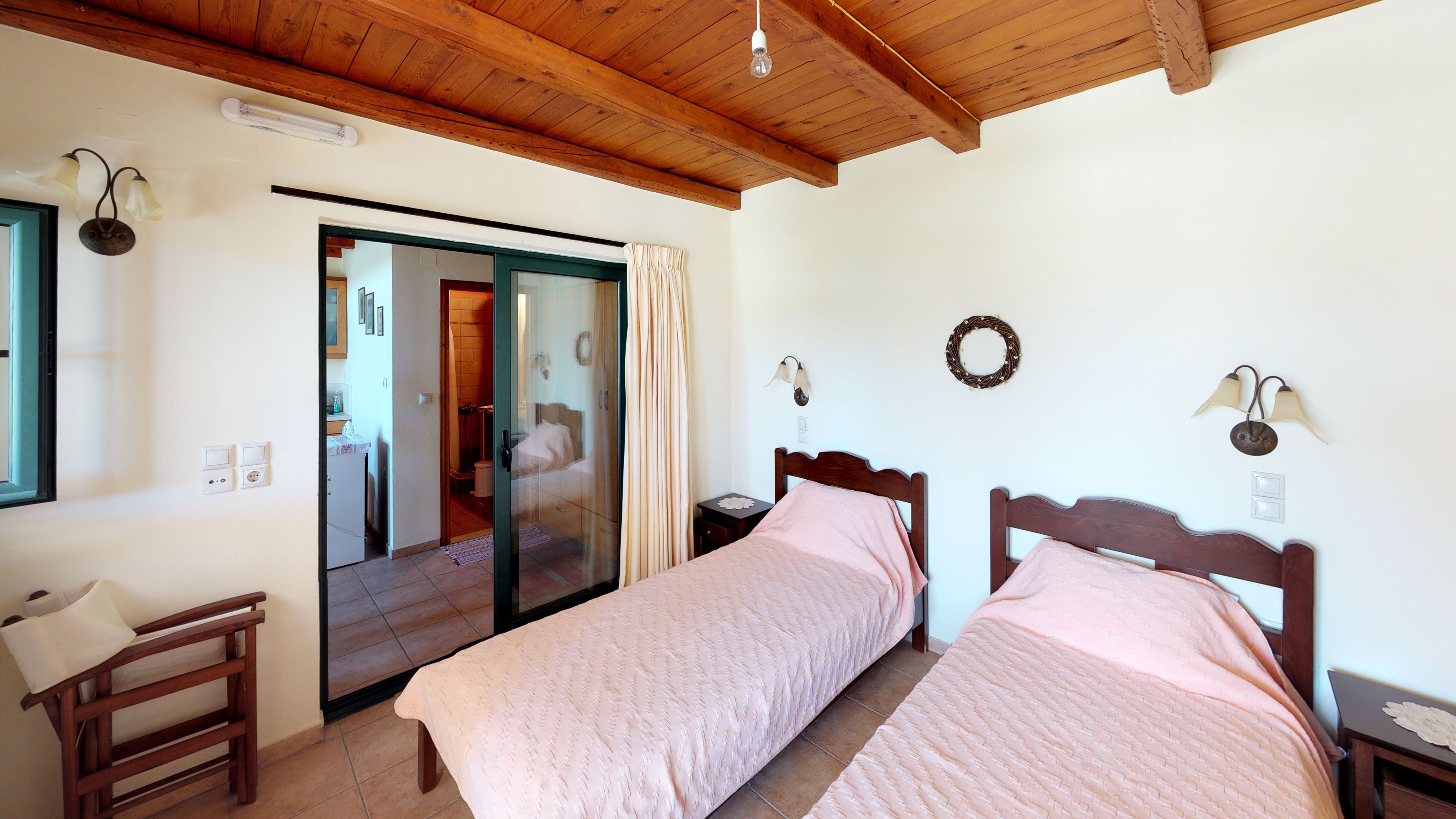 Un dormitorio con dos camas, vigas de madera en el techo, una puerta corrediza de cristal y una mesita de noche con lámpara.