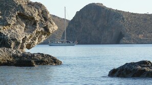 A rocky coastline with a sailboat in the distance. - Nana Apartments (Faistos)