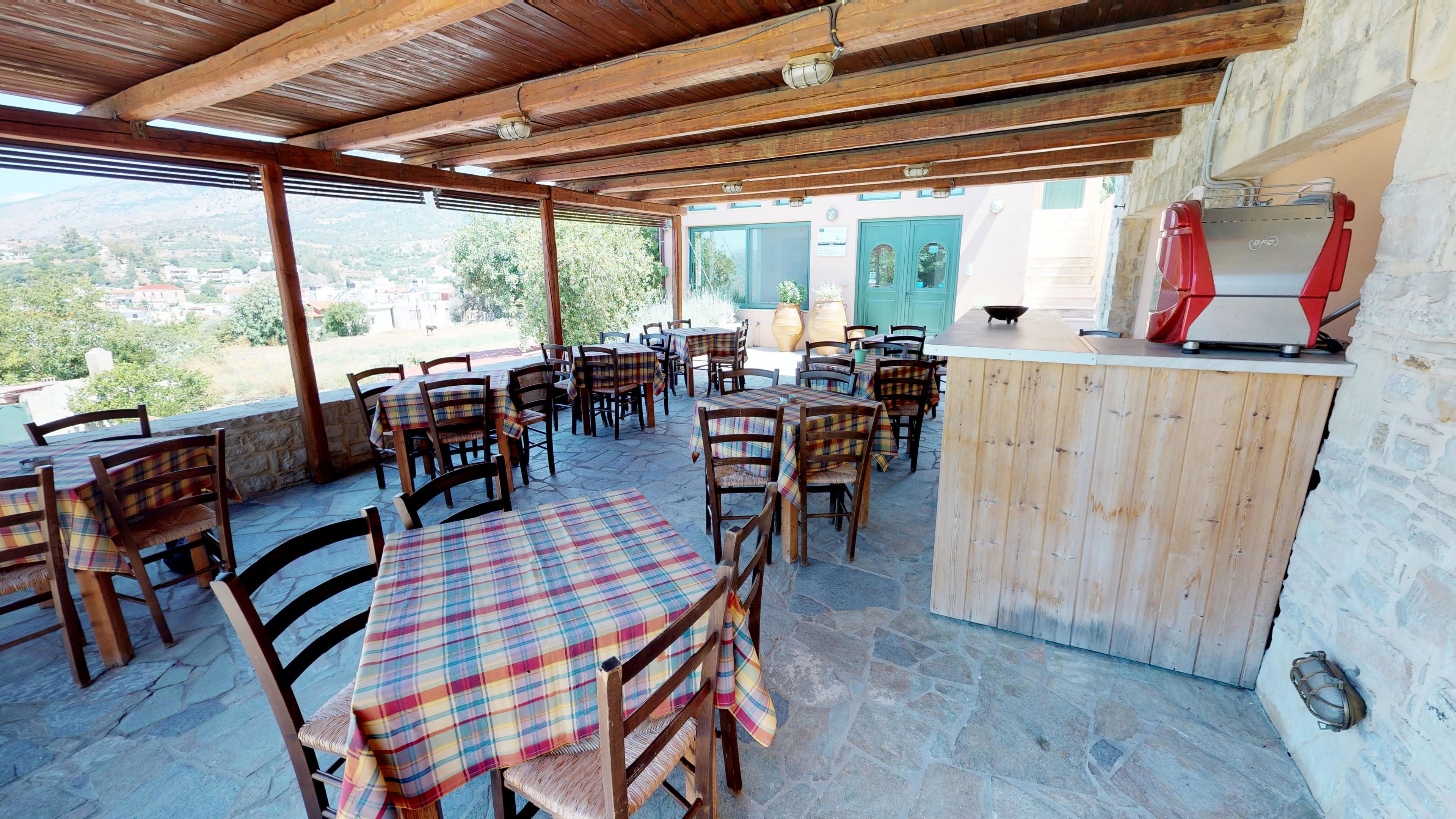 Une terrasse extérieure avec des tables et des chaises en bois, un sol en pierre et un comptoir en bois équipé d’un gril.