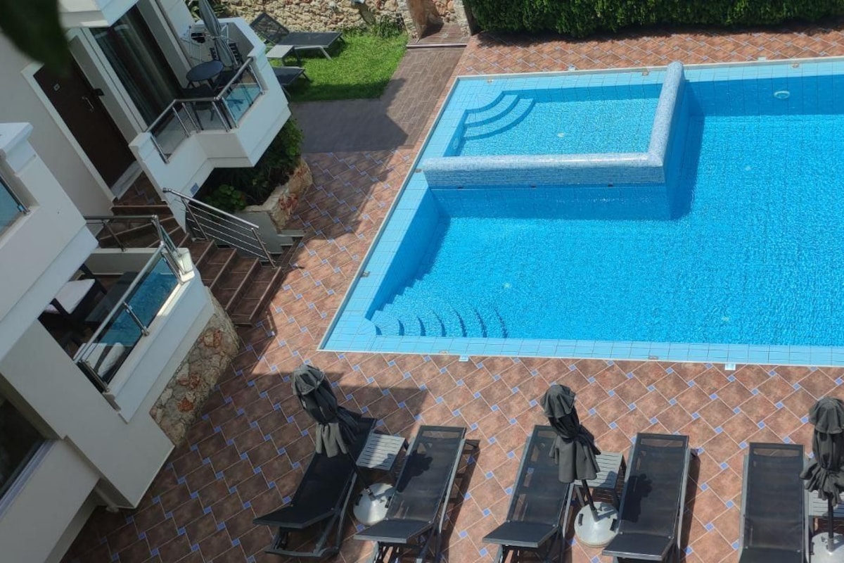Una piscina con solárium empedrado, sillas de descanso y una zona pequeña.