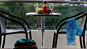 Une table avec une bouteille, des verres et des fruits, placée sur un balcon donnant sur une étendue d’eau.