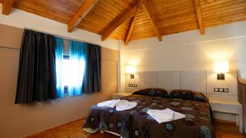 Een slaapkamer met een houten plafond, twee nachtkastjes, een bed met bloemenbedrukking en een raam met gordijnen.