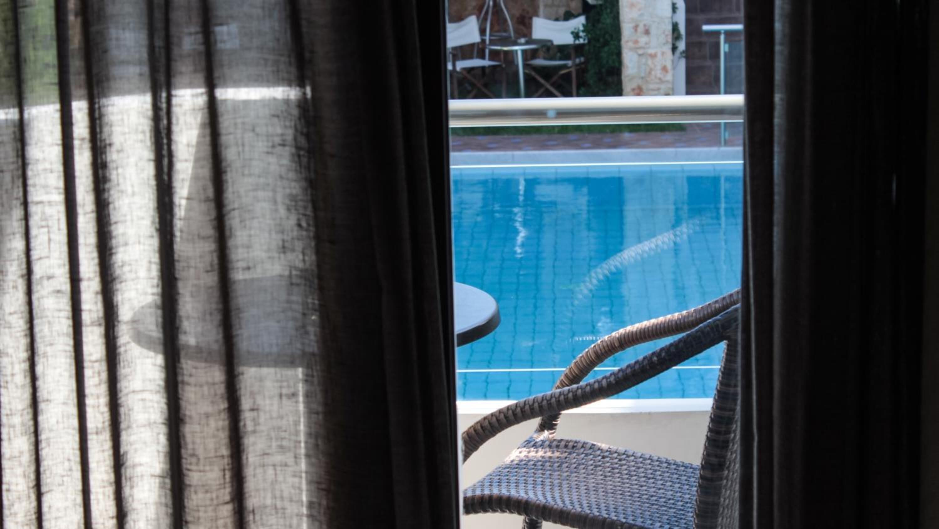 A view of a swimming pool from a window with curtains.