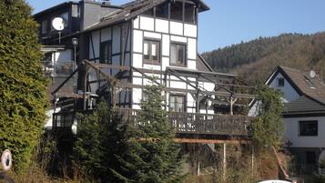 Traditional chalet-style building with a balcony and wooden staircase, situated in a mountainous area.