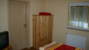 Een slaapkamer met een houten garderobe, een bed met een bedovertrek met patroon, een televisie op een houten dressoir en een raam met gordijnen.