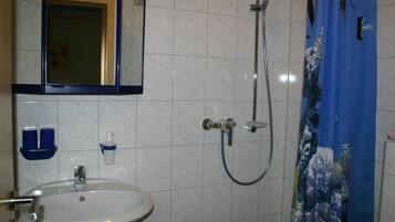 Une salle de bain avec un lavabo blanc, un miroir, une douche équipée d’un pommeau de douche à main et un rideau de douche bleu.