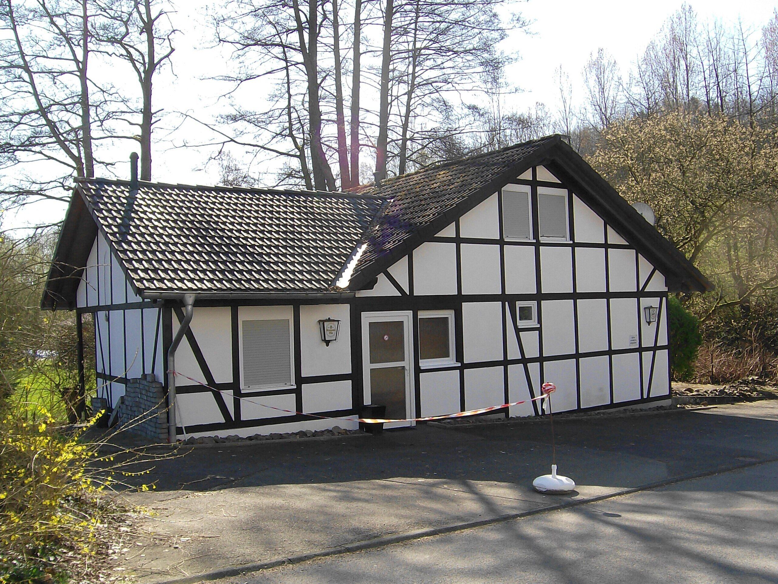 A traditional half-timbered house with a steeply pitched roof, a small porch, and a single door.