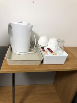 A tray with a white electric kettle, a glass, and a box containing tea bags and a spoon on a wooden table.