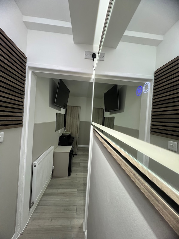A narrow hallway with a wooden floor, white walls, and a mirrored wall on one side.