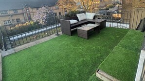 A rooftop terrace with artificial grass, a seating area, and a view of surrounding buildings. - Plaza London Hotel (London)