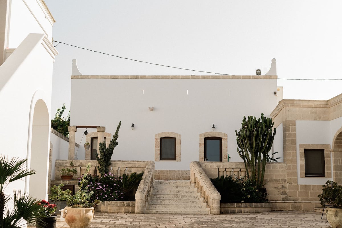 A courtyard with a white building, a staircase, and potted plants.