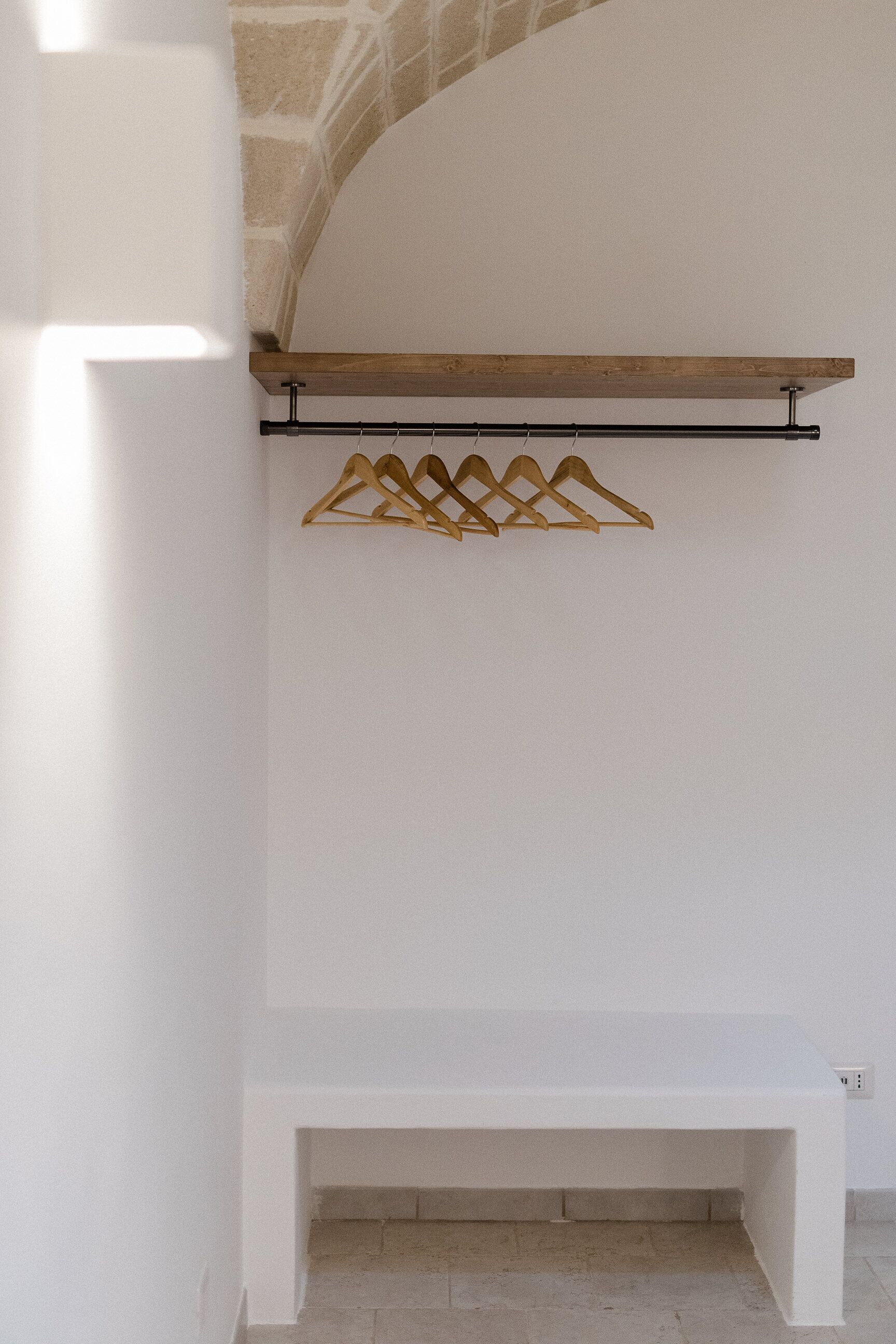 A white bench under a wooden shelf with a gold hanger rack.