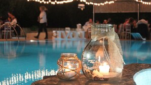 Un espace aménagé au bord de la piscine, agrémenté de guirlandes lumineuses, d’un bocal en verre contenant une bougie et d’un vase en verre avec une autre bougie.