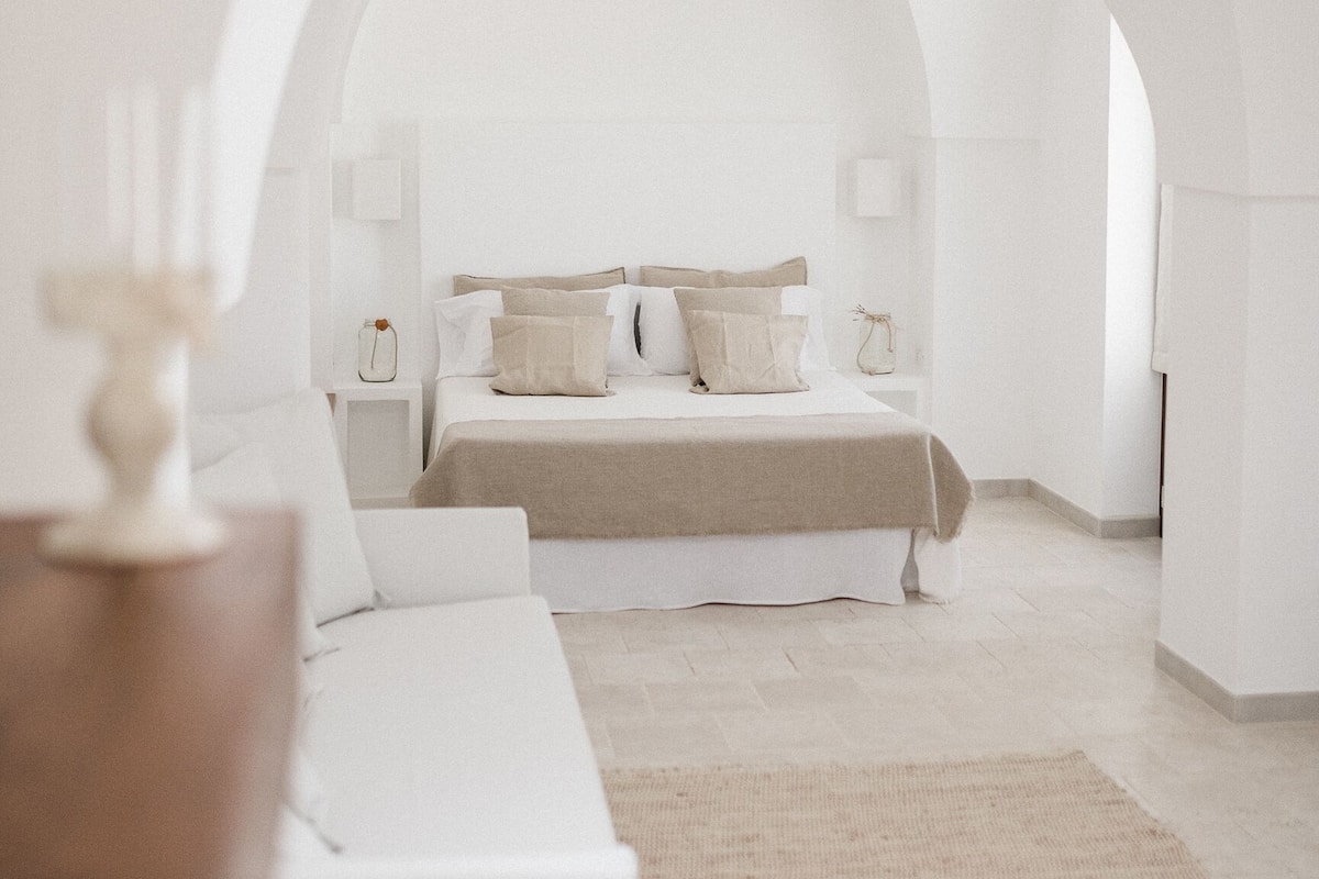 A minimalist bedroom with a bed, bedside tables, and a large arched doorway.